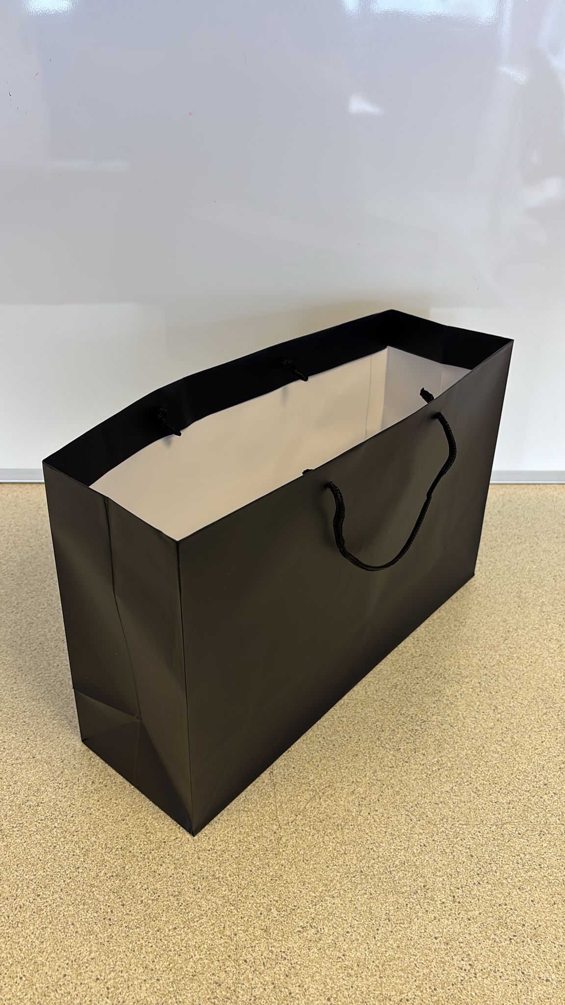 Black luxury paper carrier bag in landscape orientation with rope handles, ideal for premium retail, gifting, or branded packaging.