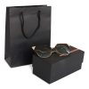 Small portrait black luxury paper gift bag with rope handles shown beside a boxed pair of sunglasses.